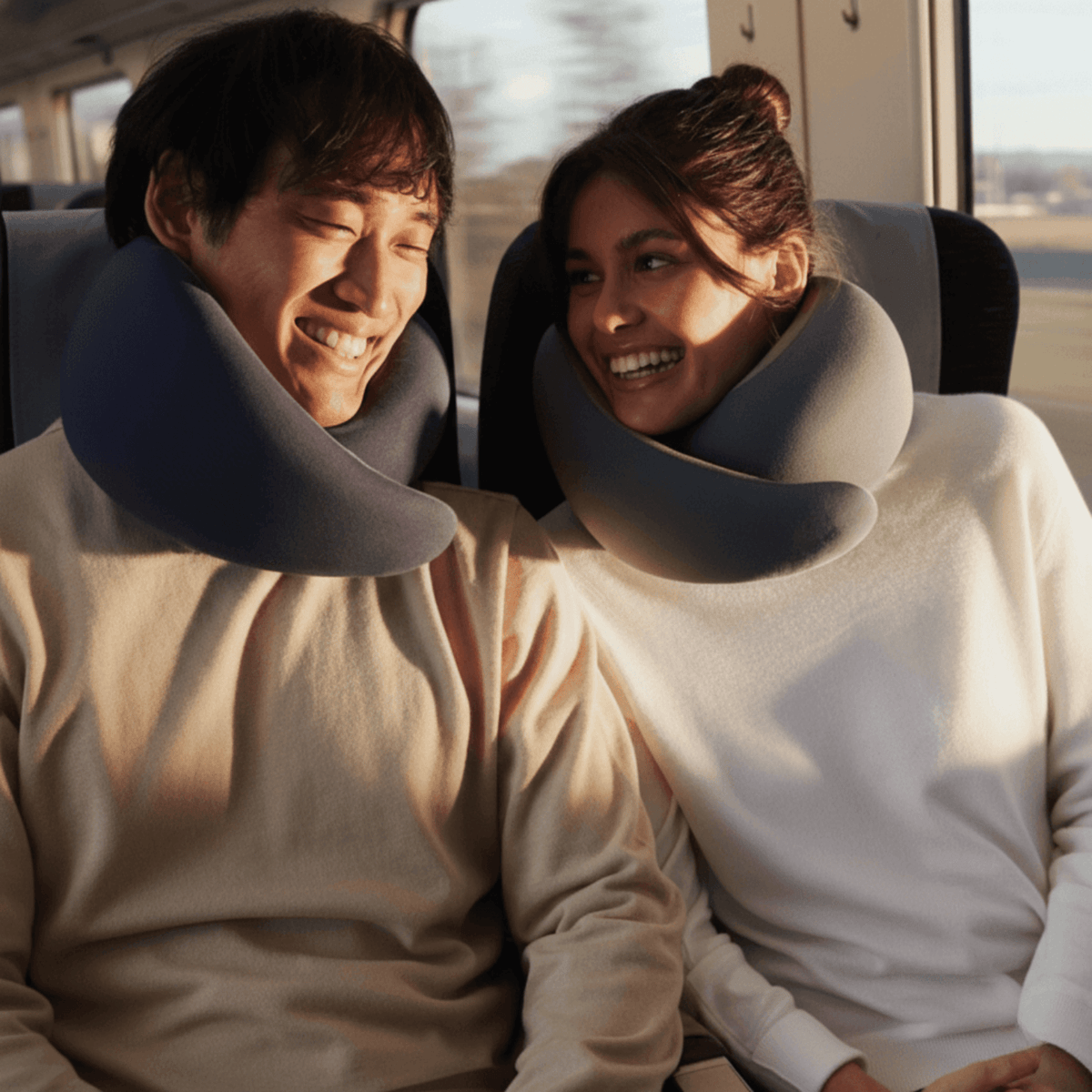 Zwei Reisende sitzen im Zug und tragen TravelFit Nackenkissen